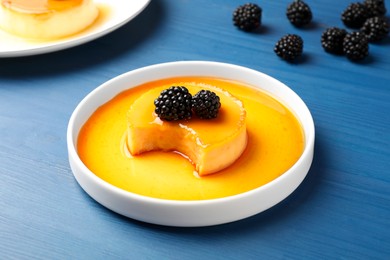 Photo of Delicious pudding with caramel and blackberries on blue wooden table