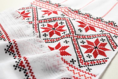 Photo of Rushnyk with traditional Ukrainian embroidery on white table, closeup. National handicraft