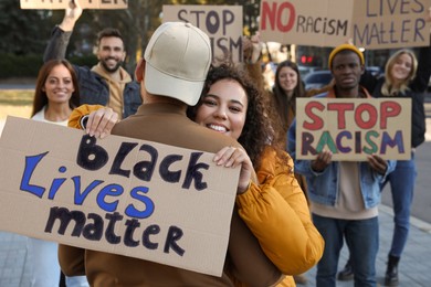 African American woman hugging man and holding sign with phrase Black Lives Matter outdoors during anti racism protest