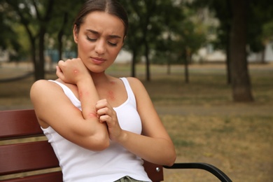 Woman scratching arm with insect bite in park. Space for text