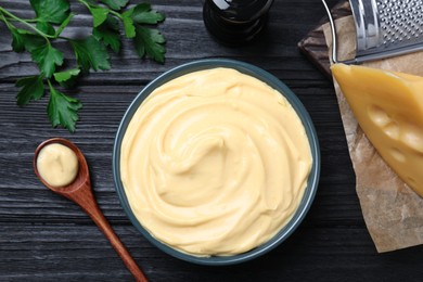 Photo of Tasty cheese sauce and parsley on black wooden table, flat lay