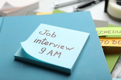 Reminder note about job interview and stationery on table, closeup