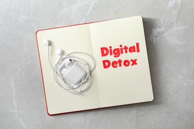 Photo of Open notebook with earphones and words DIGITAL DETOX on light grey marble background, top view