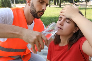Worker with bottle of water helping woman outdoors. Suffering from heat stroke