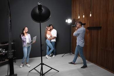 Professional photographer with assistant taking picture of young couple in modern studio