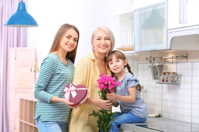 Beautiful mature lady, daughter and grandchild with gifts in kitchen. Happy Women's Day