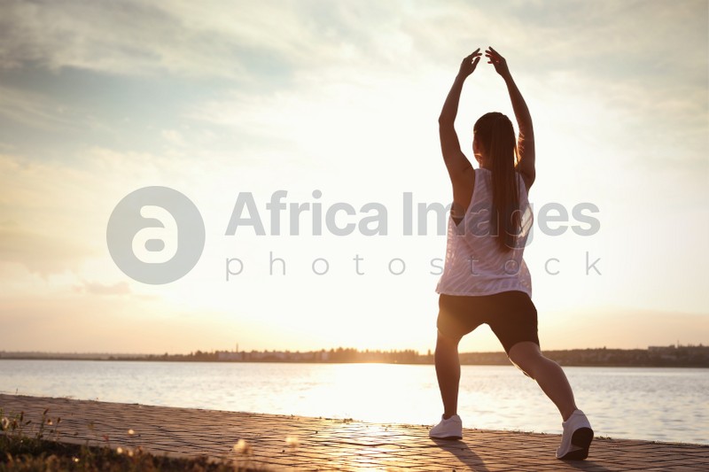 Young woman doing exercise near river in morning. Space for text