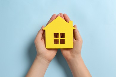 Woman holding house figure on light blue background, top view