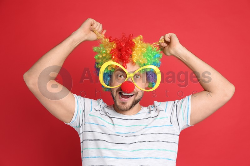 Funny man with large glasses, rainbow wig and clown nose on red background. April fool's day