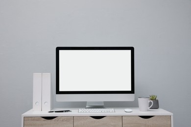 Comfortable workplace with blank computer display on desk near light grey wall. Space for text