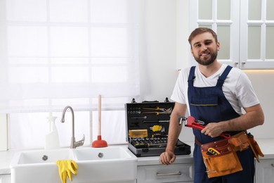 Professional plumber with plunger and instruments near sink in kitchen