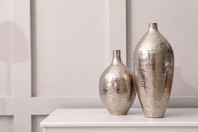 Shiny vases on white table indoors, space for text. Interior element