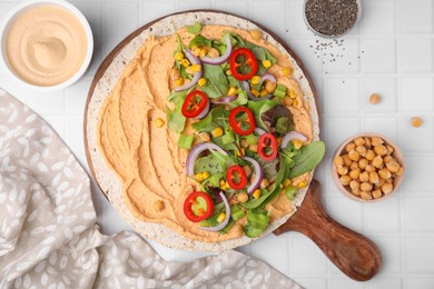 Photo of Tortilla with hummus and vegetables on white table, flat lay