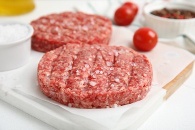 Raw hamburger patty with salt on white table, closeup