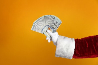 Santa holding dollar bills on orange background, closeup