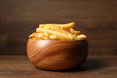 Delicious fresh french fries in bowl on wooden table, closeup