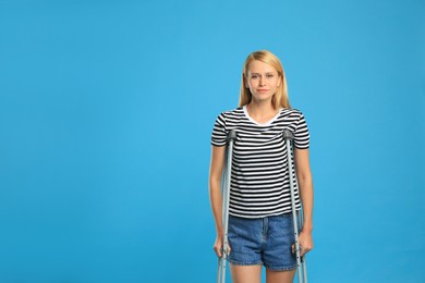 Young woman with axillary crutches on light blue background, space for text