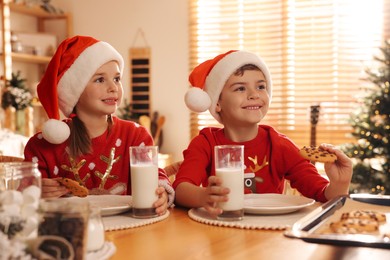 Cute little children eating delicious Christmas cookies at home