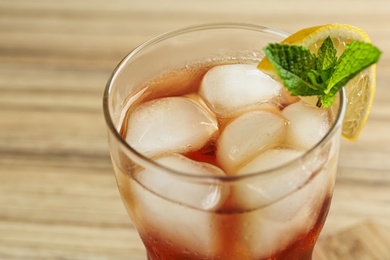 Glass of tasty ice tea with lemon and mint on wooden table, closeup