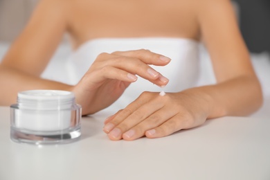 Woman applying moisturizing cream at white table, closeup
