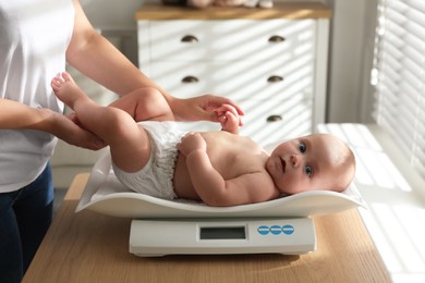 Young woman weighting her cute baby at home, closeup. Health care