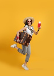 Happy female tourist with passport, ticket and suitcase on yellow background