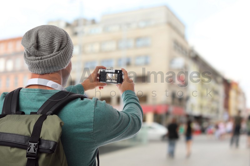 Traveler with backpack taking photo in foreign city during vacation, back view