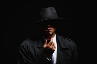 Old fashioned detective with smoking pipe on dark background
