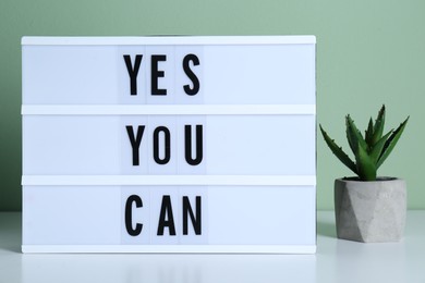 Lightbox with phrase Yes You Can and potted houseplant on table against light green background. Motivational quote
