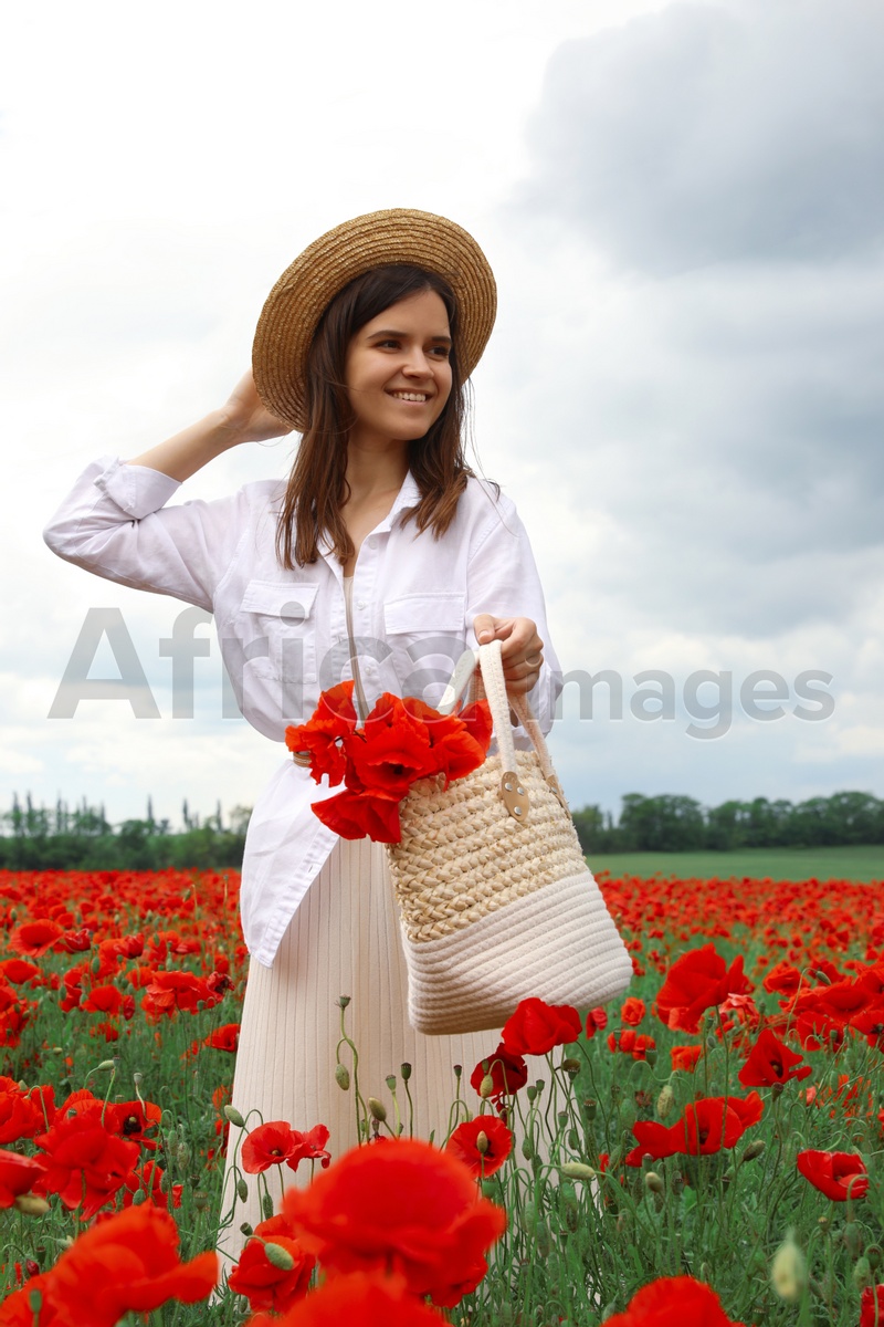 Photo of Woman holding handbag with poppy flowers in beautiful field