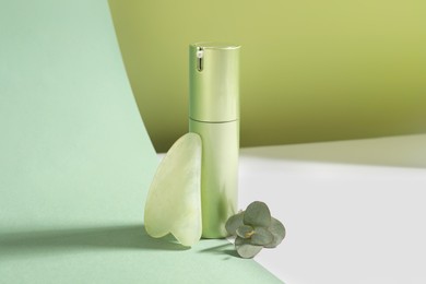 Photo of Jade gua sha tool, eucalyptus branch and cosmetic product on color background