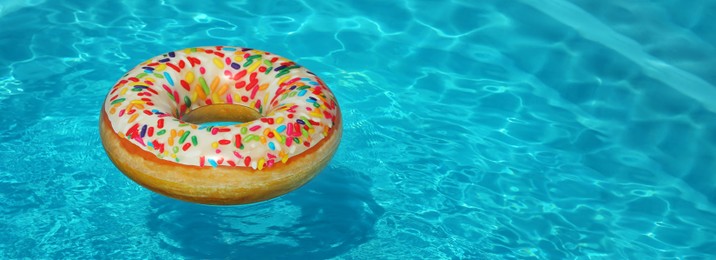 Bright inflatable doughnut ring floating in swimming pool on sunny day, space for text. Banner design