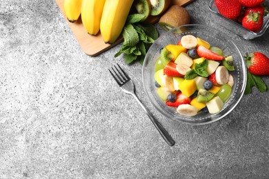 Delicious fresh fruit salad in bowl on grey table, flat lay. Space for text