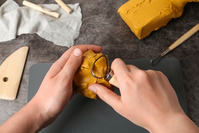 Woman working with loop tool and clay at grey stone table, closeup