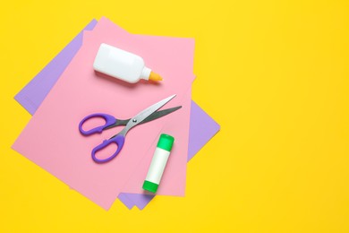Glue, colorful paper and scissors on yellow background, flat lay. Space for text