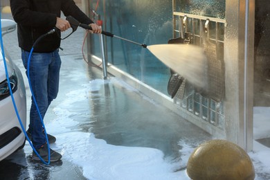 Man cleaning auto mats with high pressure water jet at self-service car wash, closeup