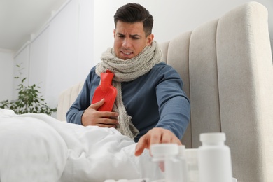 Ill man with hot water bottle taking pills from bedside table at home