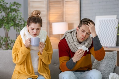 Couple suffering from cold together on sofa at home