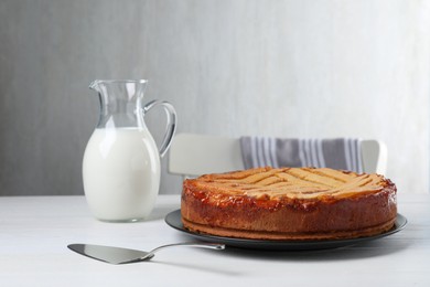 Tasty apricot pie and jug of milk on white wooden table