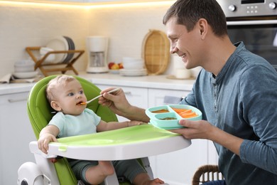 Father feeding his cute little baby in kitchen