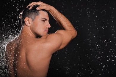 Man washing hair while taking shower on black background. Space for text