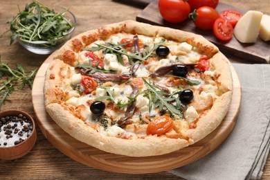 Photo of Tasty pizza with anchovies and ingredients on wooden table