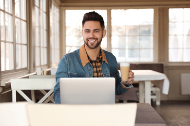 Young blogger with laptop drinking latte at table in cafe