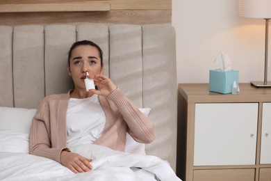 Sick young woman using nasal spray in bed at home