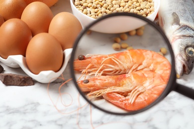 Different products with magnifier focused on shrimps, closeup. Food allergy concept
