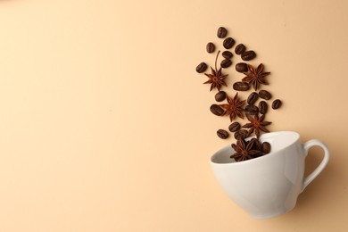Photo of Coffee beans and anise stars falling into cup on beige background, flat lay. Space for text