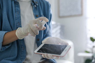 Woman applying antibacterial spray onto smartphone indoors, closeup