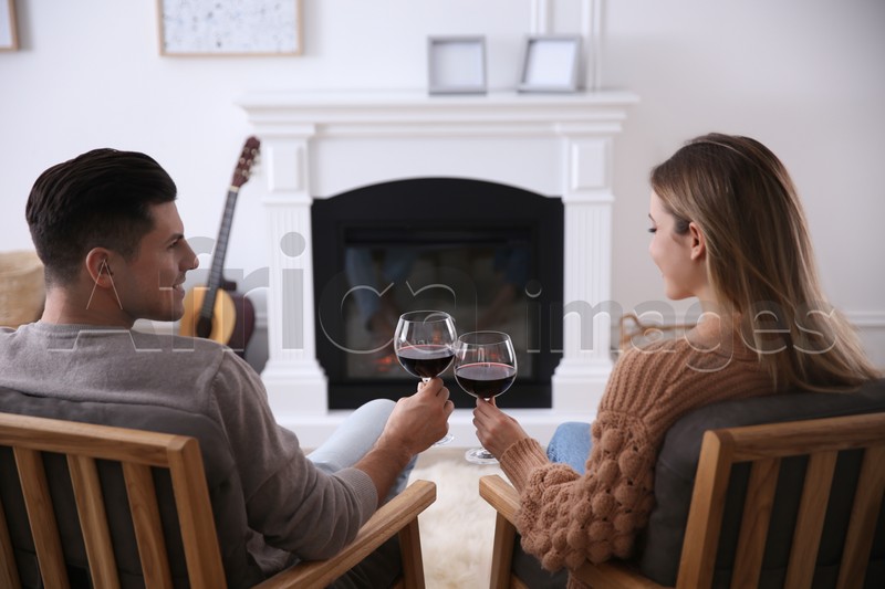 Happy couple toasting with glasses of wine near fireplace at home