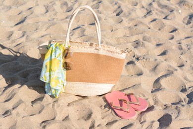 Straw bag with beach wrap, sunglasses and flip flops on sand. Summer accessories