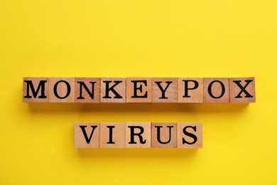 Photo of Words Monkeypox Virus made of wooden cubes on yellow background, top view